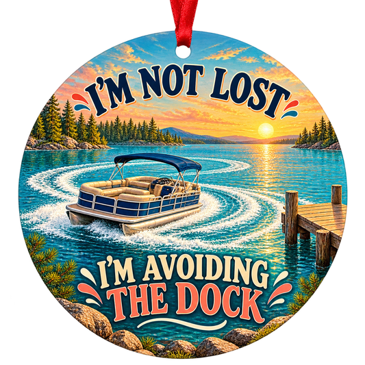 A blue pontoon boat circles a turquoise lake beside a wooden dock at sunset. Round ornament with red hanging ribbon.
