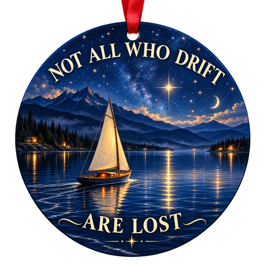 An ivory-sailed boat glides across a deep-blue lake beneath stars and a crescent moon. Round ornament with red hanging ribbon.